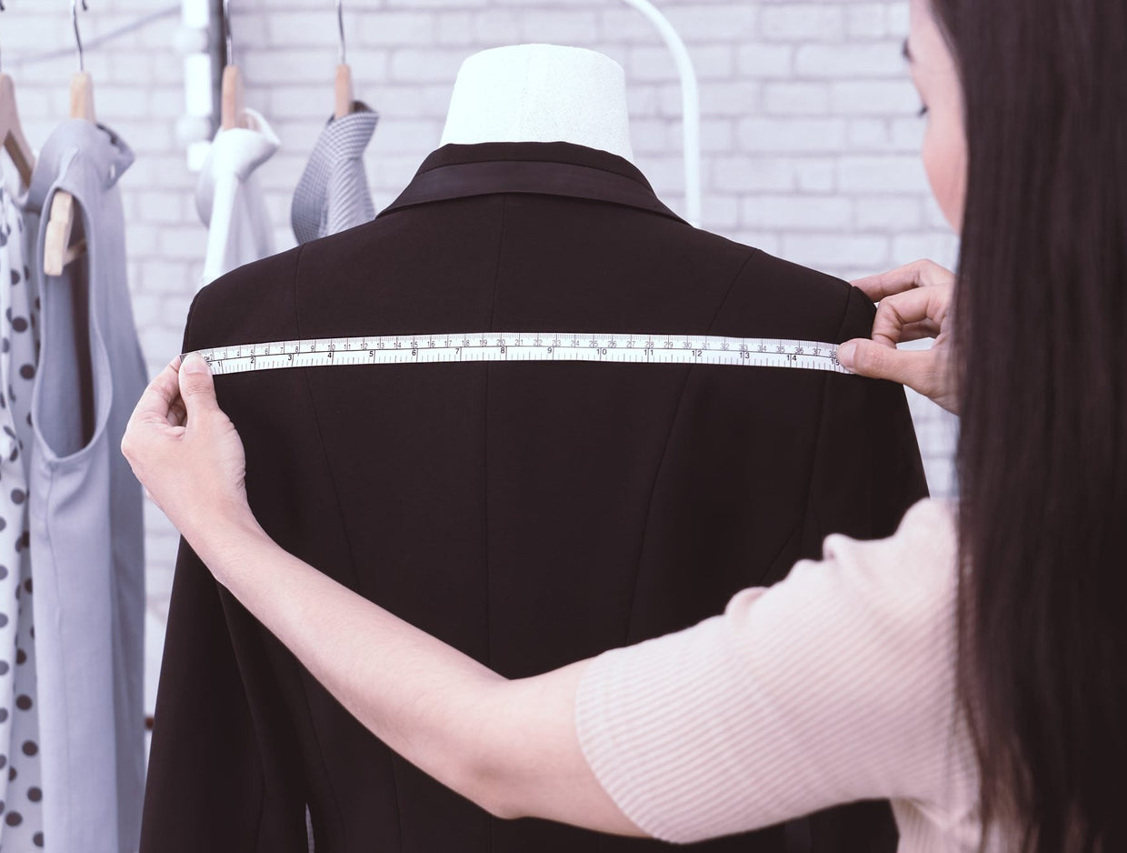 Tailor measuring across the shoulders of a dark jacket on a dress form with a tape measure
